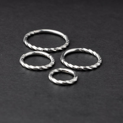 Four stainless steel twisted hoops in different sizes displayed on a dark background, emphasizing their intricate twisted texture.