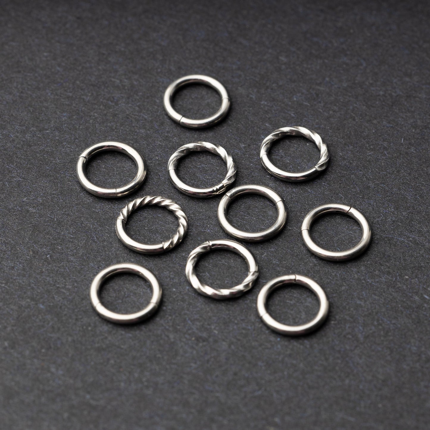 Set of silver clicker rings with smooth and twisted designs, displayed on a dark background.