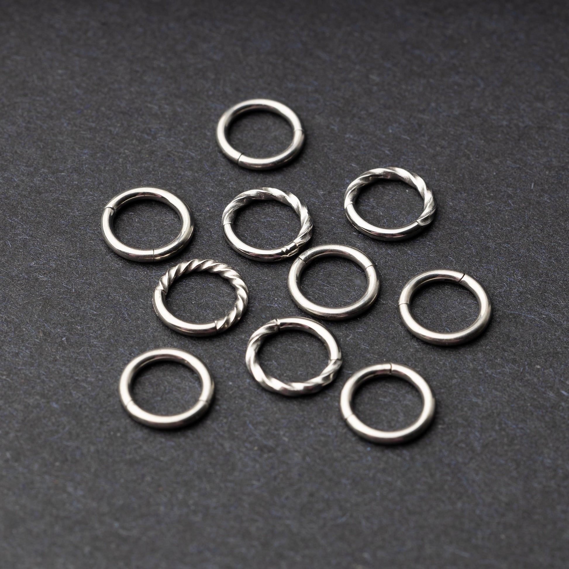 Set of silver clicker rings with smooth and twisted designs, displayed on a dark background.