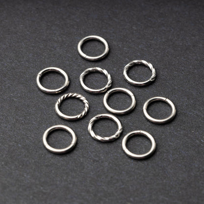 Set of silver clicker rings with smooth and twisted designs, displayed on a dark background.