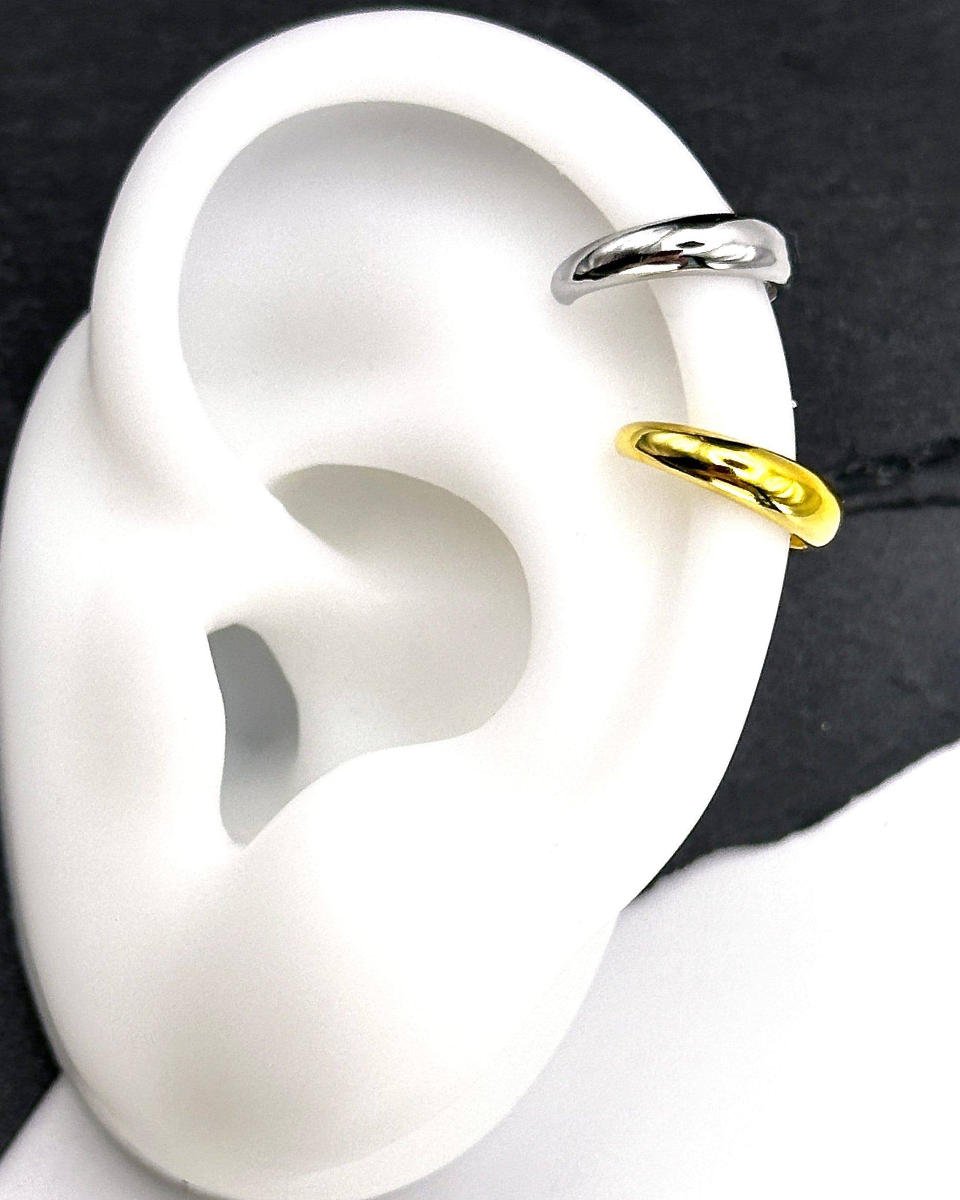Bold ear cuffs in silver and gold finishes with a smooth, domed design, shown on a display ear.