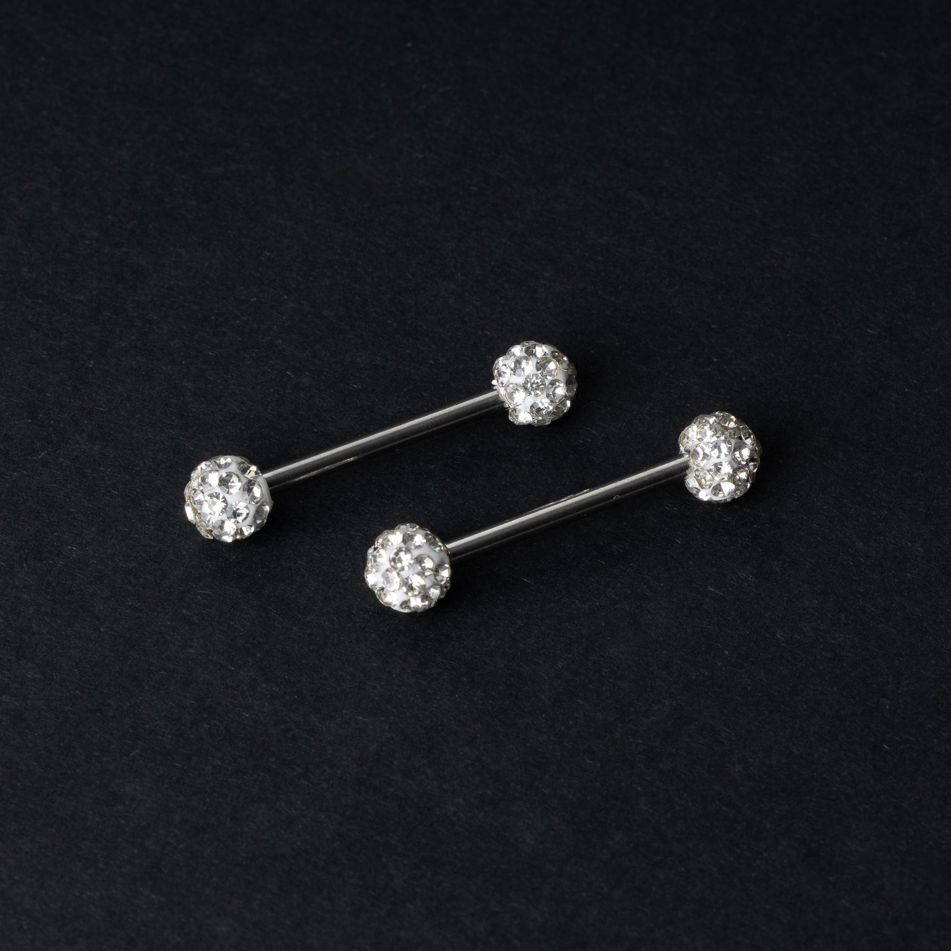 Barbells with textured crystal-encrusted ends in silver displayed on a dark background.
