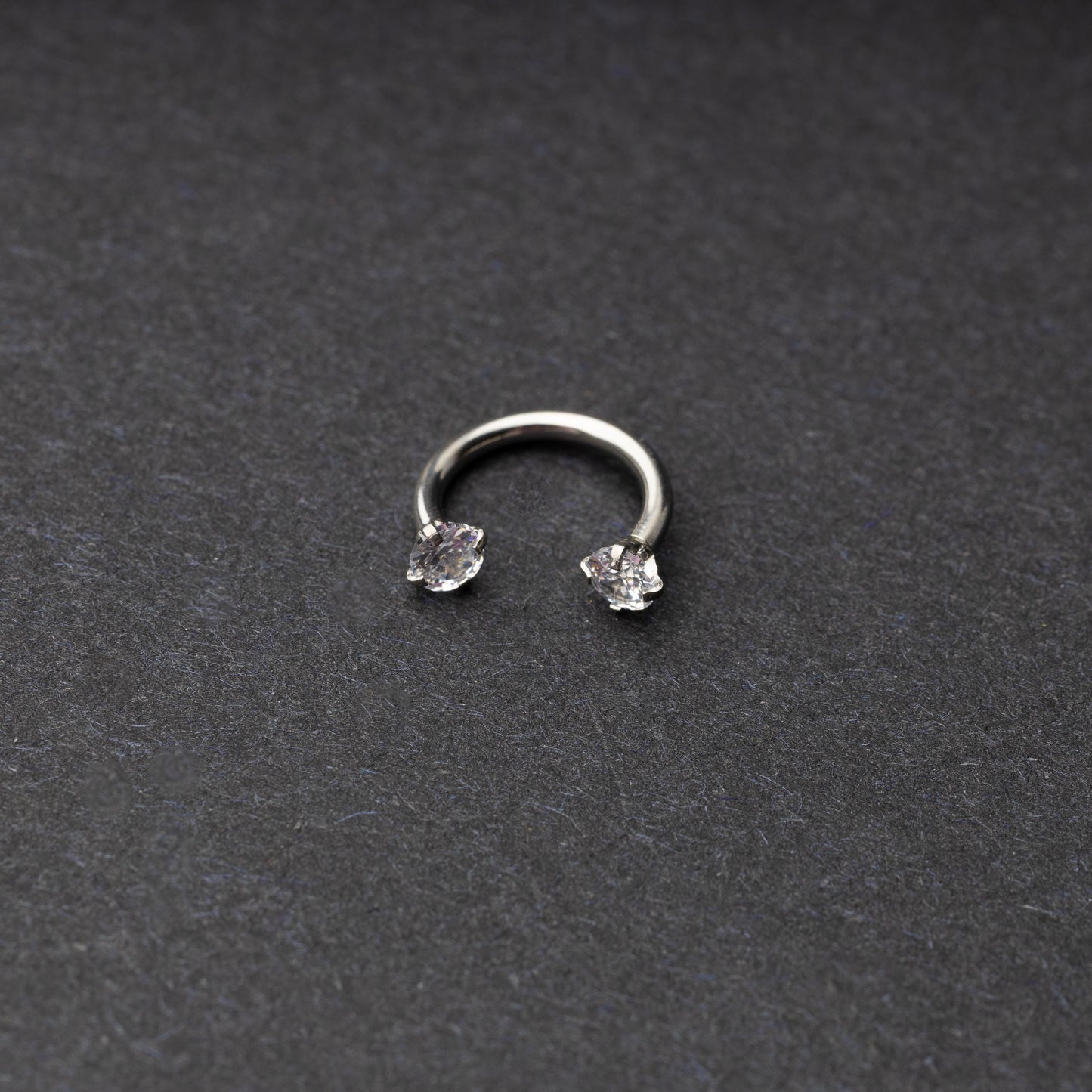 A silver jewelled horseshoe hoop with gemstone ends, displayed on a dark background.