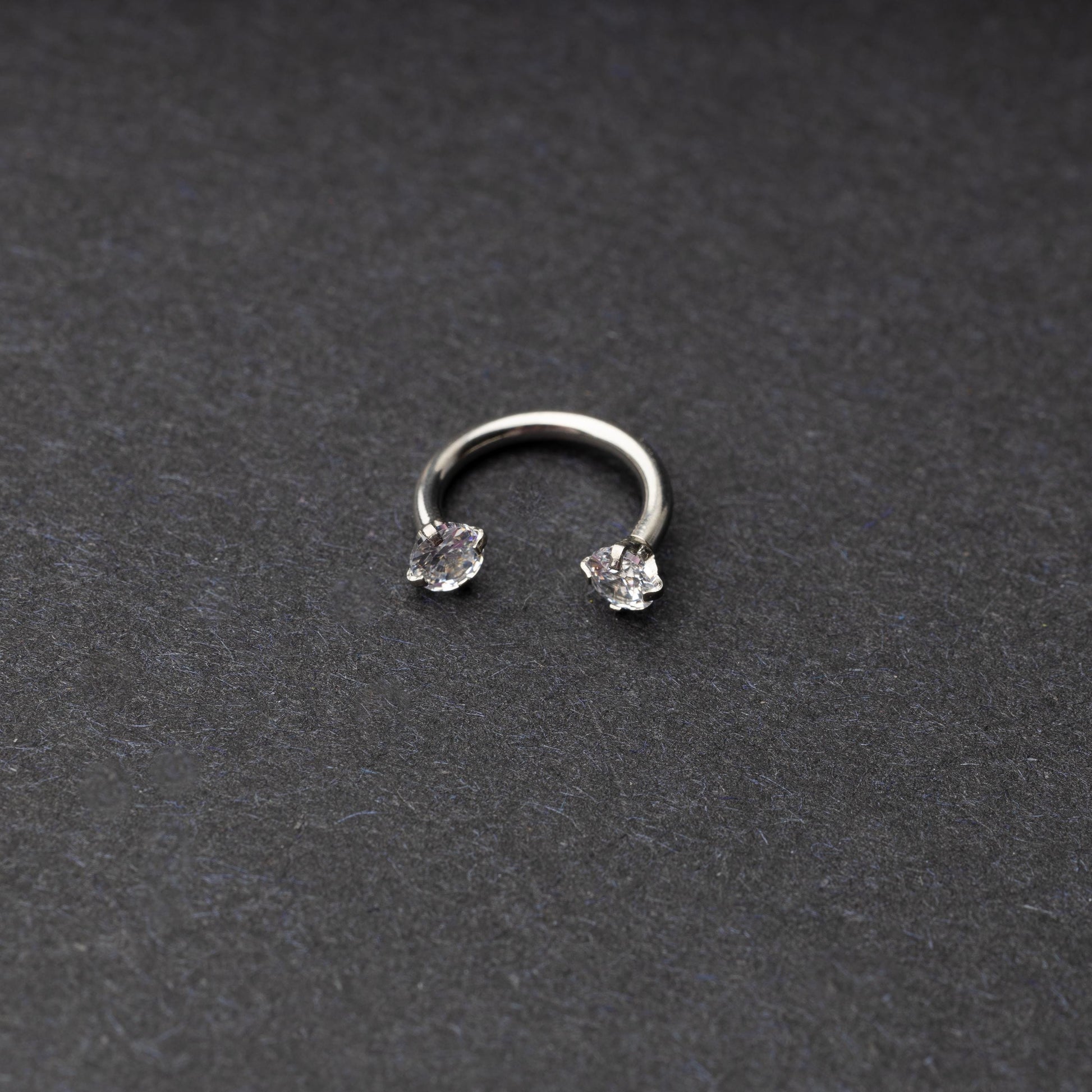 A silver jewelled horseshoe hoop with gemstone ends, displayed on a dark background.