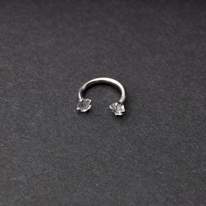 A silver jewelled horseshoe hoop with gemstone ends, displayed on a dark background.