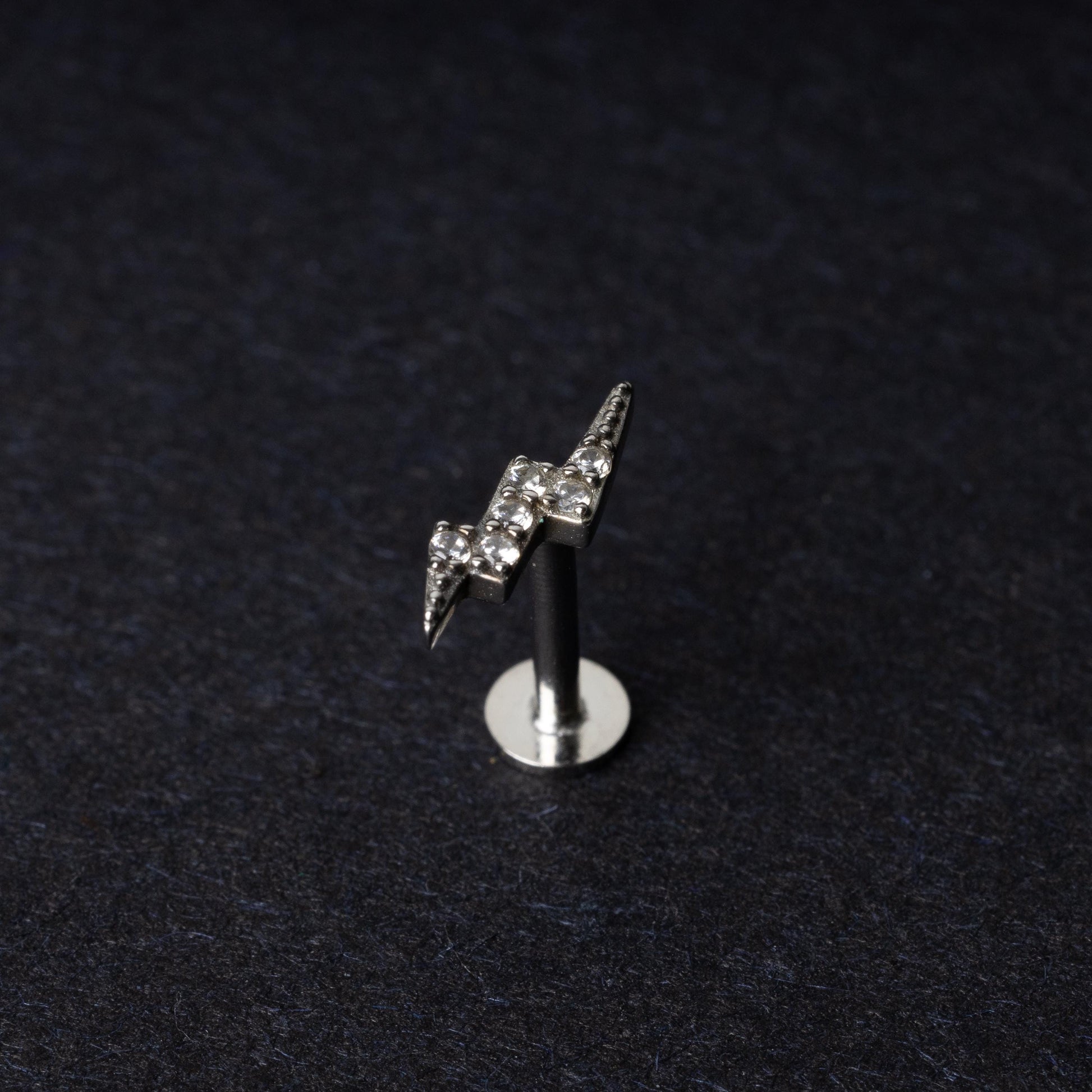 Silver lightning bolt labret stud with crystal detailing, displayed on a dark background.
