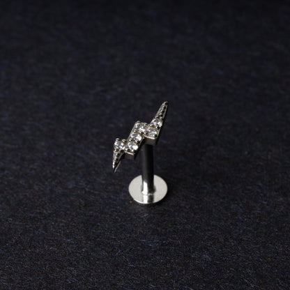 Silver lightning bolt labret stud with crystal detailing, displayed on a dark background.