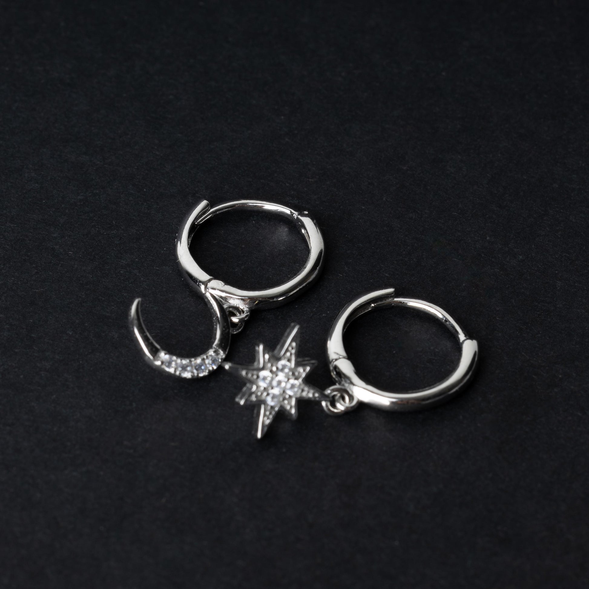 Silver moon and star hoop earrings with cubic zirconia accents, displayed on a dark background.