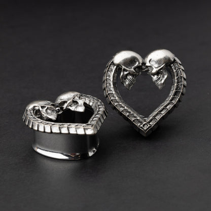 Heart-shaped tunnel plugs with intricate skull details and textured edges, displayed on a dark background.