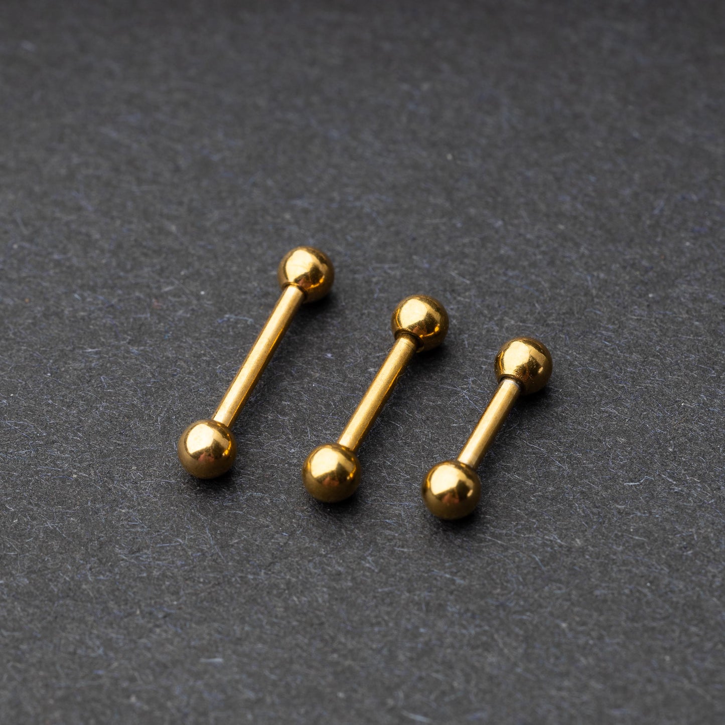 Gold-tone stainless steel barbells with polished spheres on a dark background.