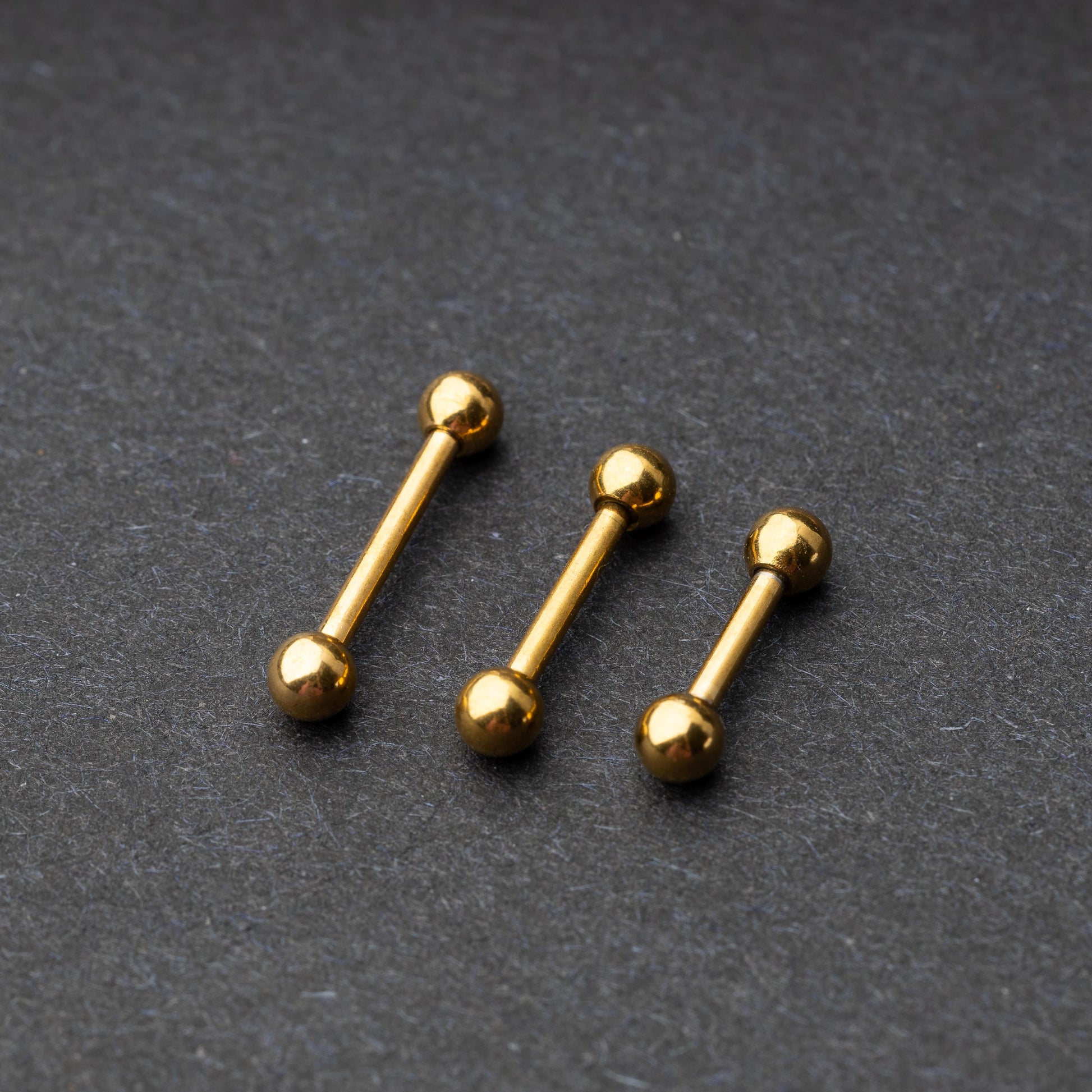Gold-tone stainless steel barbells with polished spheres on a dark background.