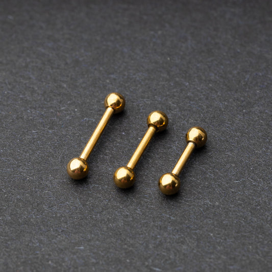 Gold-tone stainless steel barbells with polished spheres on a dark background.