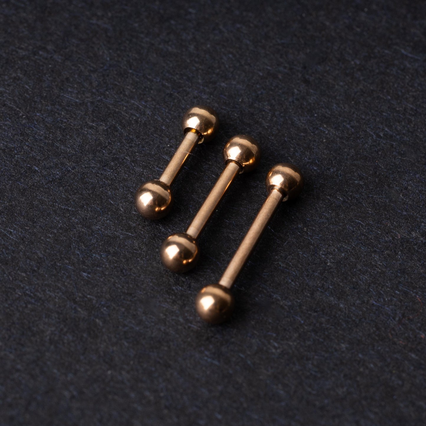 Rose Gold-tone stainless steel barbells on a dark background.