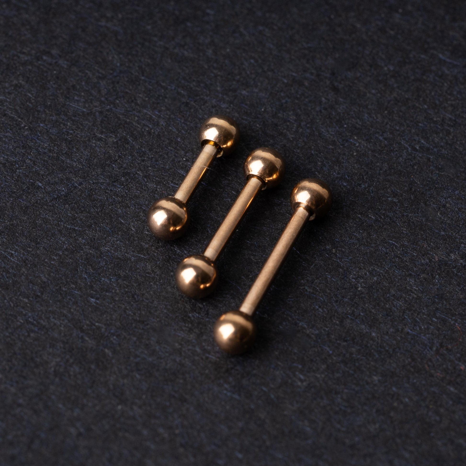 Rose Gold-tone stainless steel barbells on a dark background.