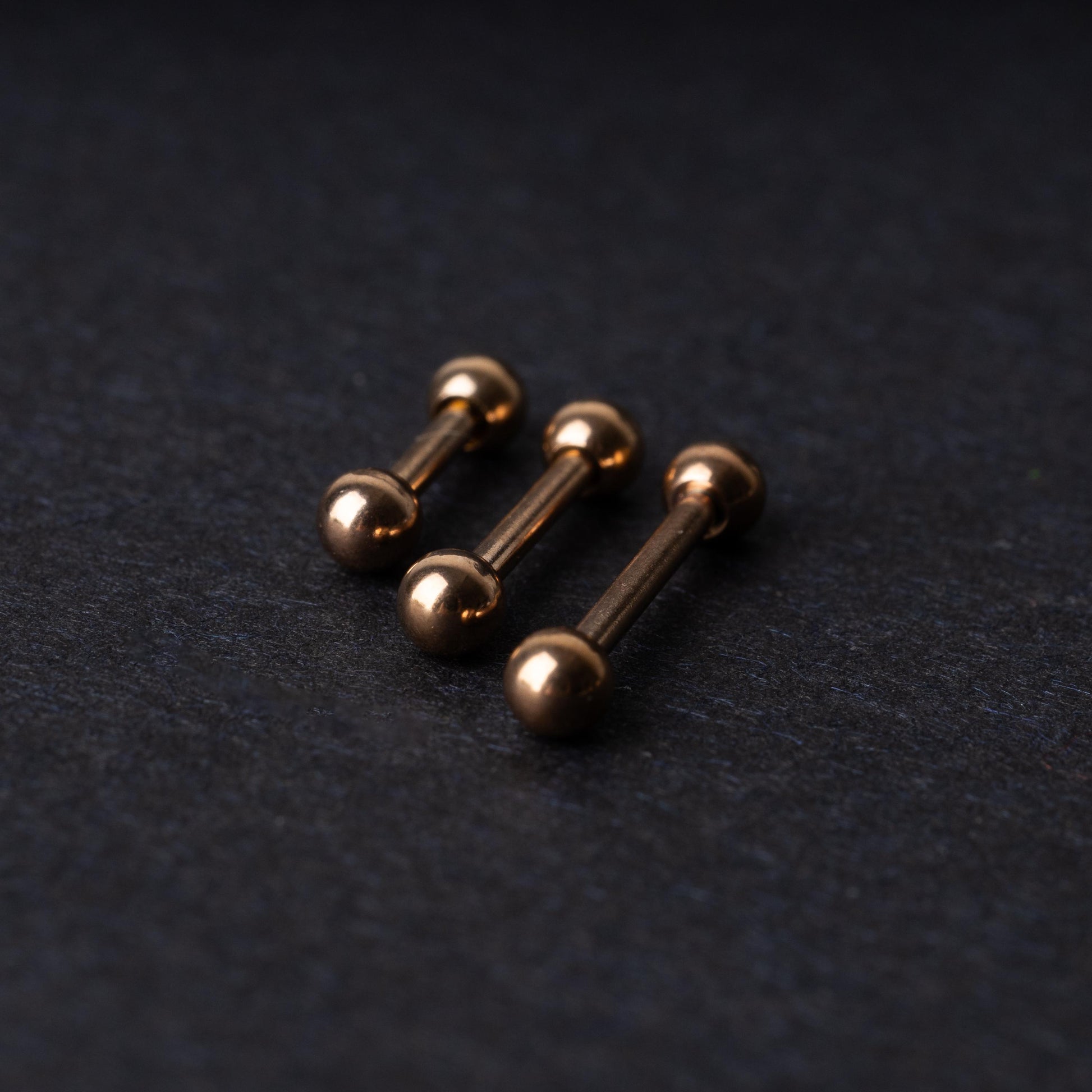 Rose Gold-tone stainless steel barbells on a dark background.
