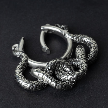 One open snake ear weight in polished silver, featuring detailed scales and a seamless hinge closure, displayed on a dark background.
