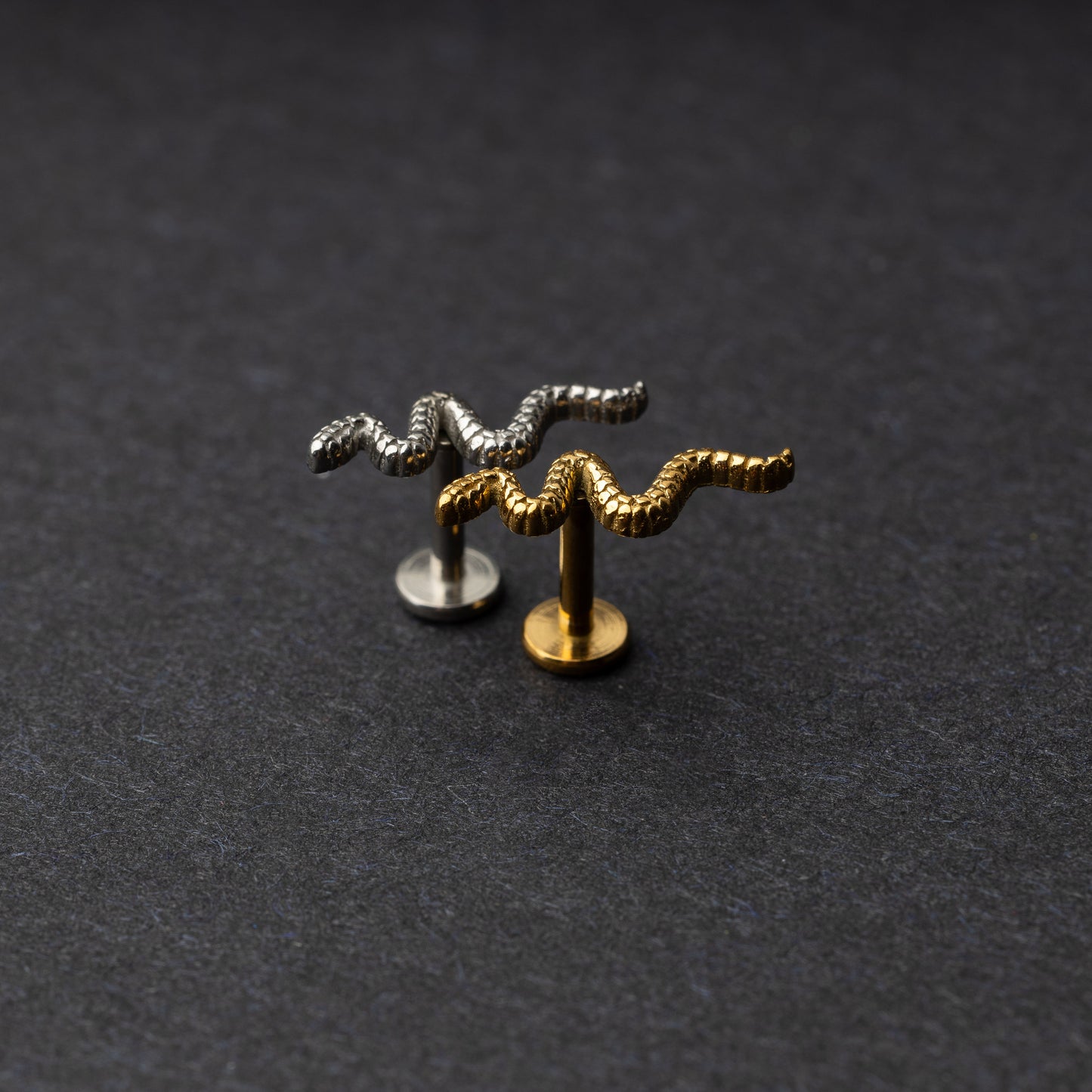 Silver and gold snake motif labrets made of stainless steel displayed on a dark background.