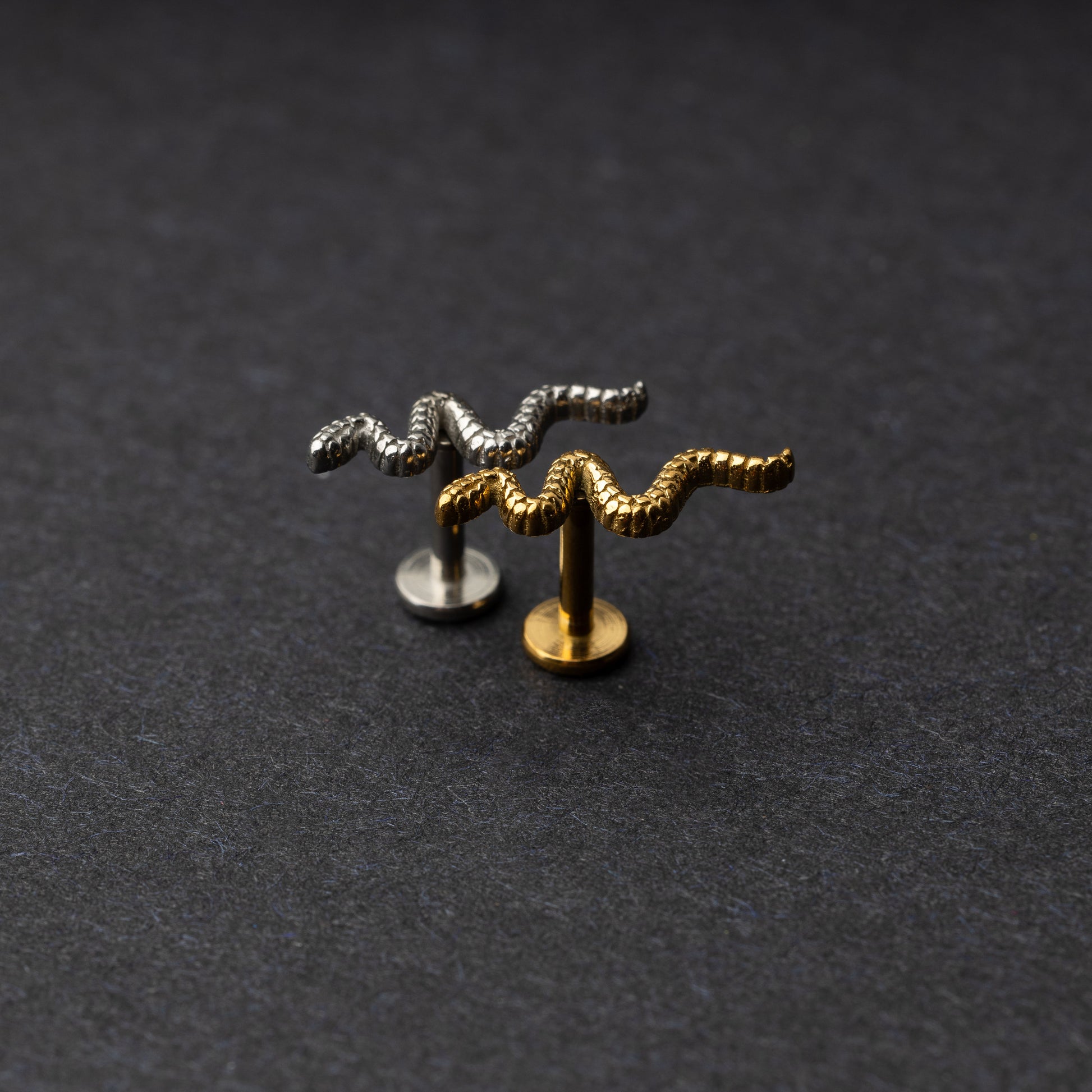 Silver and gold snake motif labrets made of stainless steel displayed on a dark background.