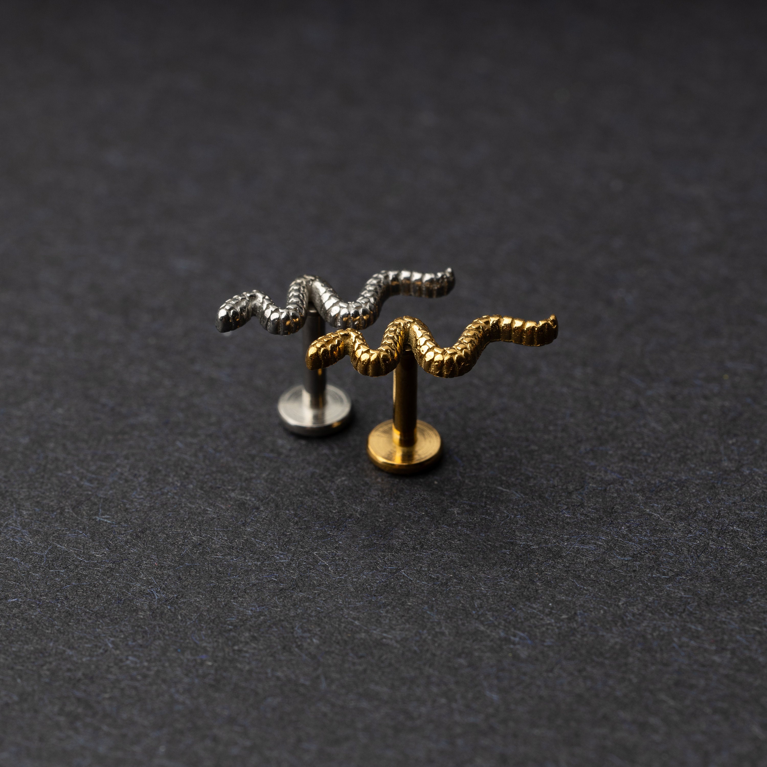 Silver and gold snake motif labrets made of stainless steel displayed on a dark background.