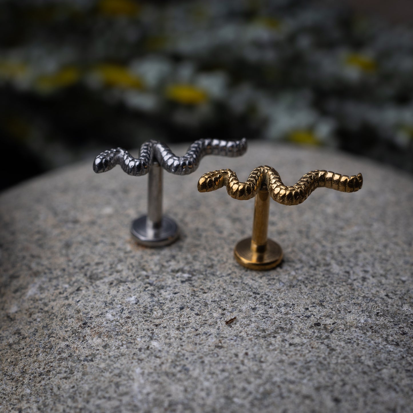 Silver and gold snake motif labrets made of stainless steel displayed on a dark background.