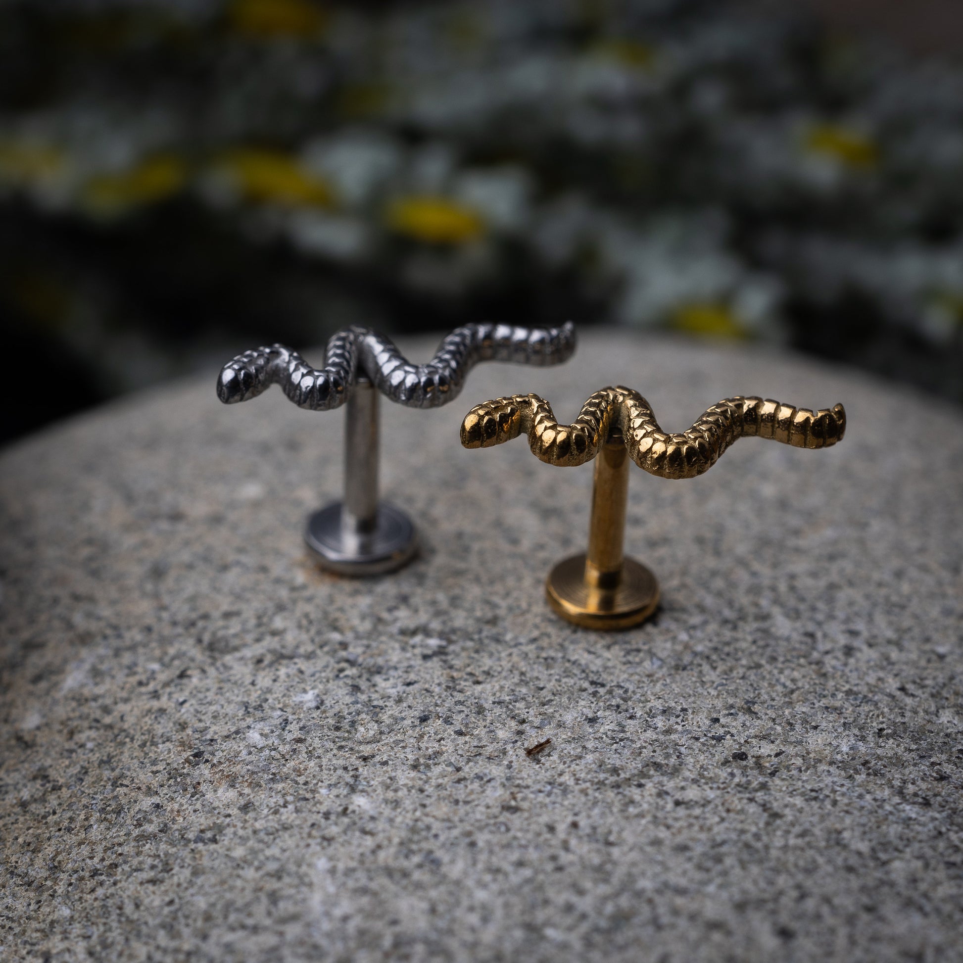 Silver and gold snake motif labrets made of stainless steel displayed on a dark background.