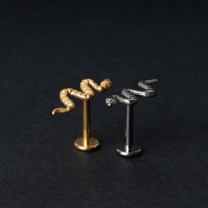Gold-tone and silver-tone snake labret bars with intricate coiled snake designs displayed on a dark background.

