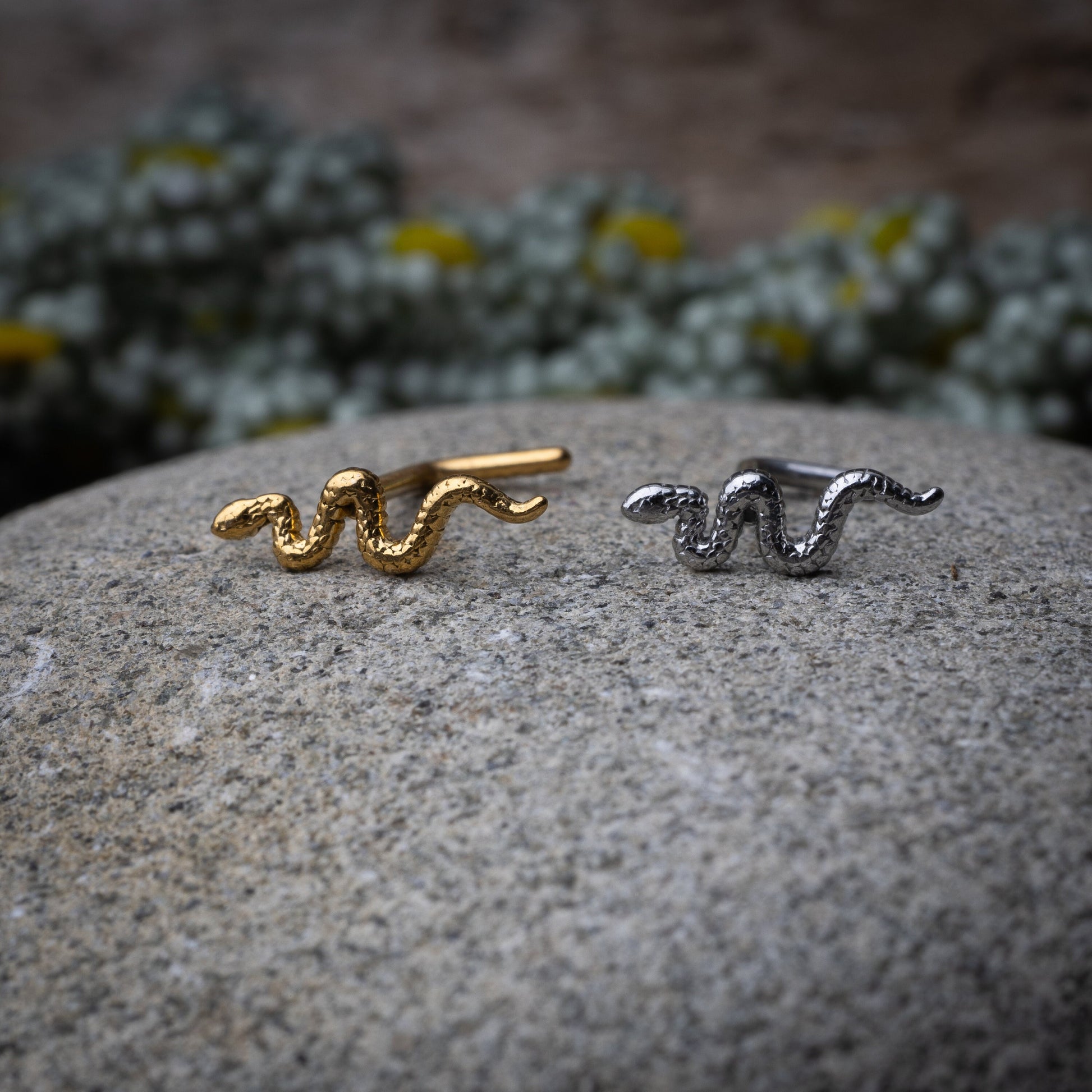 Snake-shaped nose studs in gold and silver finishes displayed on a dark background.