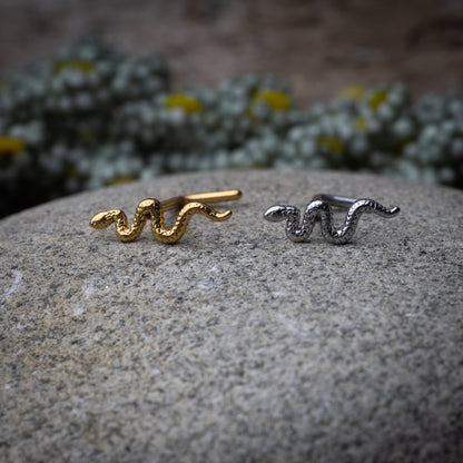 Snake-shaped nose studs in gold and silver finishes displayed on a dark background.