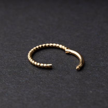 Close-up of a gold rope-textured septum clicker on a dark background, showcasing its intricate design and open hinge mechanism.