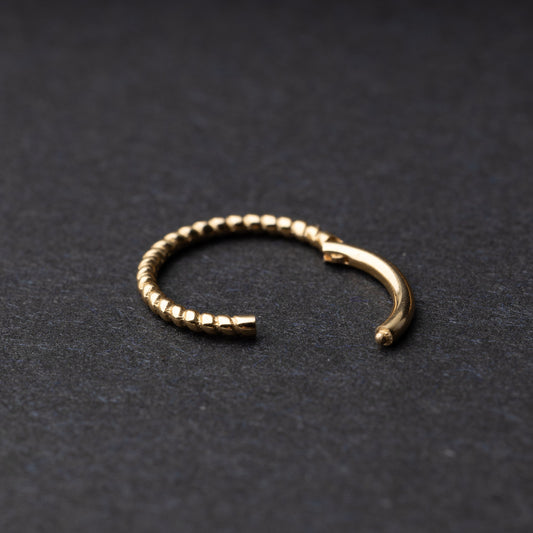 Close-up of a gold rope-textured septum clicker on a dark background, showcasing its intricate design and open hinge mechanism.