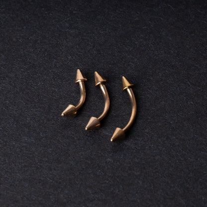 Three gold-tone titanium curved barbells with cone ends, displayed on a dark textured background, showcasing their sleek curved design and polished finish.