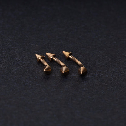 Three gold-tone titanium curved barbells with cone ends, displayed on a dark textured background, showcasing their sleek curved design and polished finish.