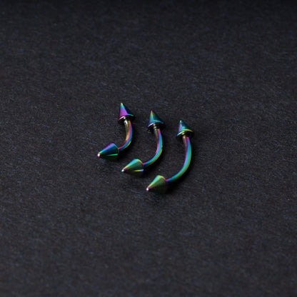 Three rainbow titanium curved barbells with cone-shaped ends, displayed on a dark textured background, showcasing their vivid color gradient and sleek design.
