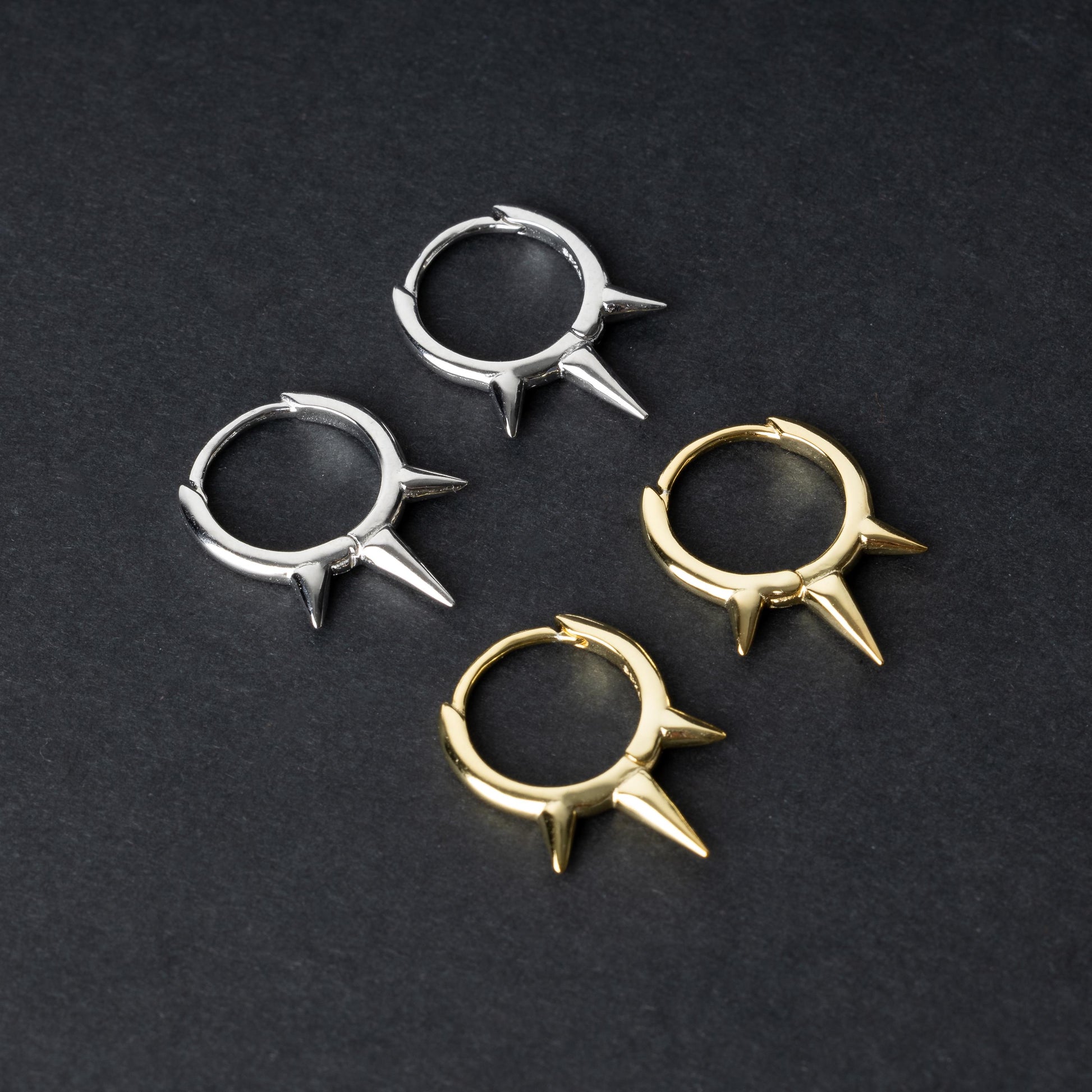 Pair of sterling silver and gold spiked clicker rings with three evenly spaced spikes, displayed on a dark textured background.