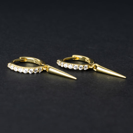 Gold hoop earrings with crystal detailing and a pointed spike charm, displayed on a dark background.