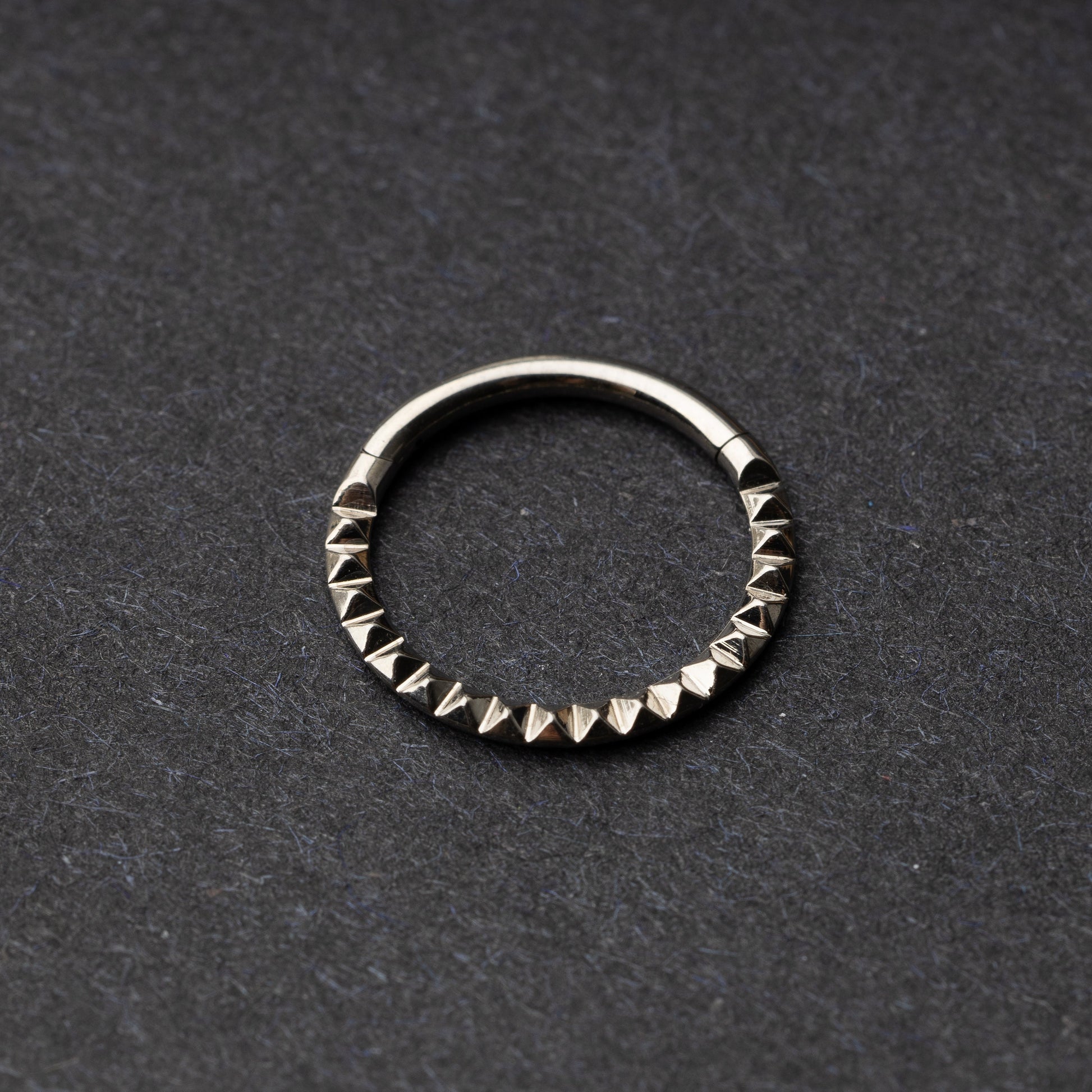 Spiked titanium clicker ring on a dark background.