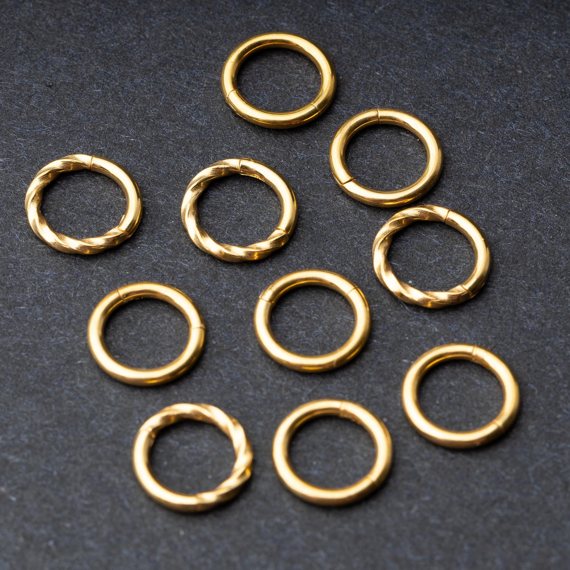 Set of gold clicker rings with smooth and twisted designs, displayed on a dark background.