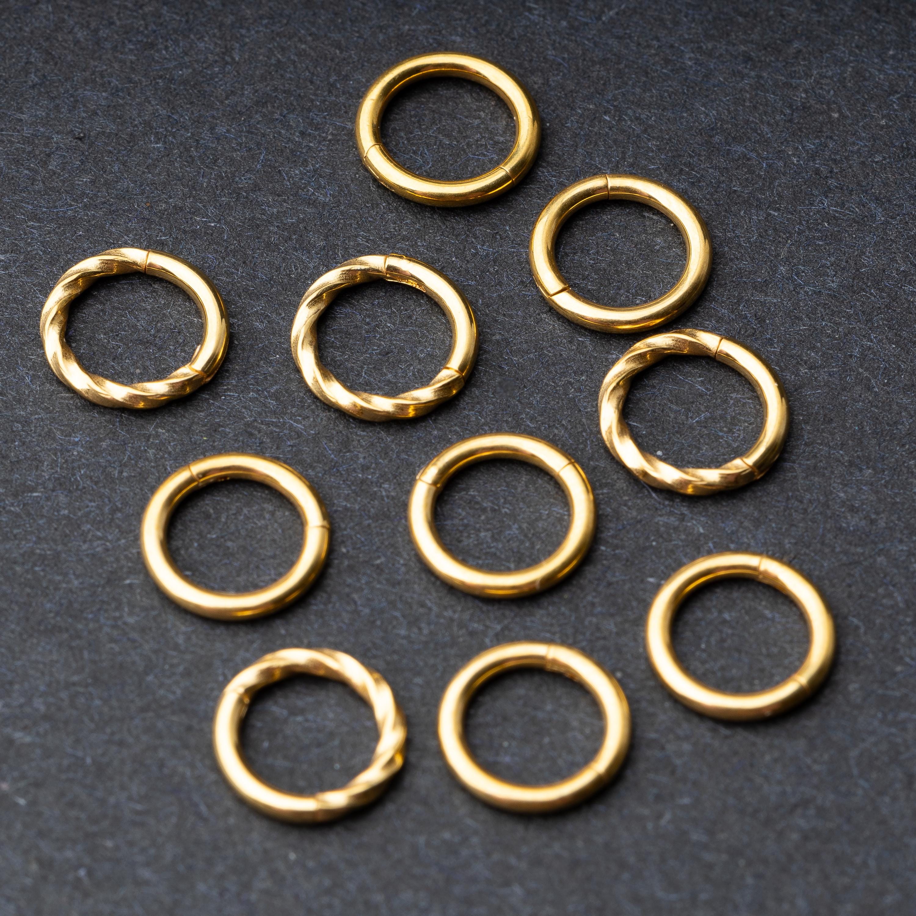 Set of gold clicker rings with smooth and twisted designs, displayed on a dark background.