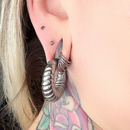 Stackable twisted clicker rings displayed in a models ear alongside a larger hanging ear gauge. 