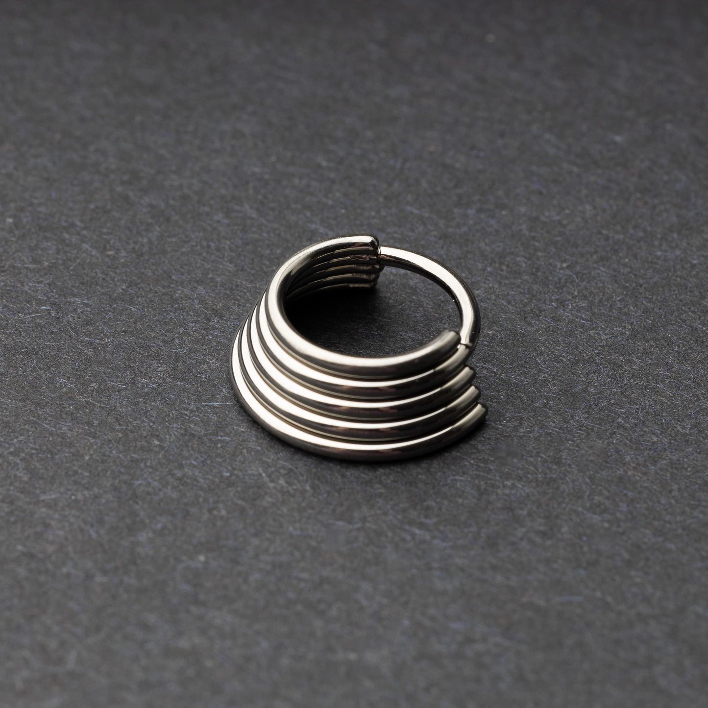 A silver-tone septum clicker with a stacked multi-ring design, displayed on a dark background, showcasing its bold and modern style.

