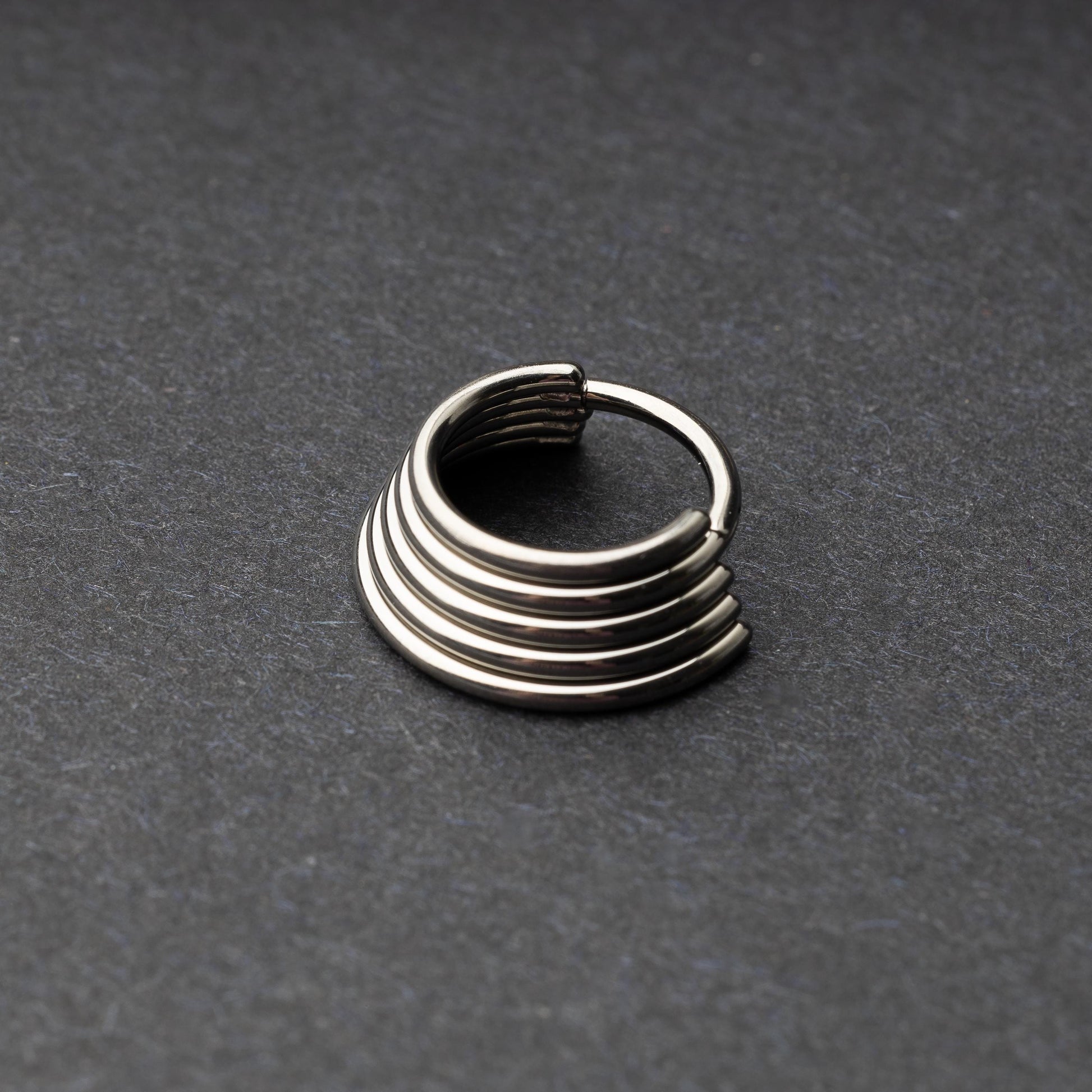 A silver-tone septum clicker with a stacked multi-ring design, displayed on a dark background, showcasing its bold and modern style.

