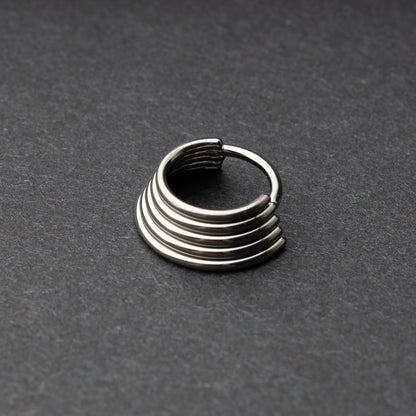 A silver-tone septum clicker with a stacked multi-ring design, displayed on a dark background, showcasing its bold and modern style.

