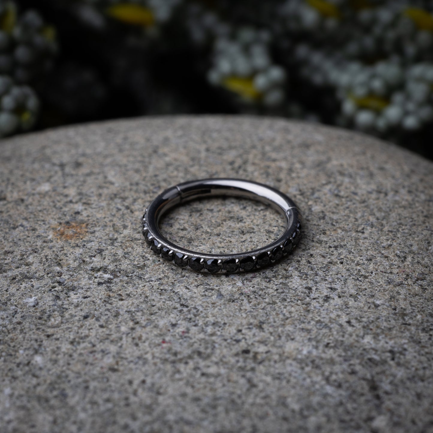 A textured stainless steel seamless ring with a polished finish, placed on a stone, textured background.