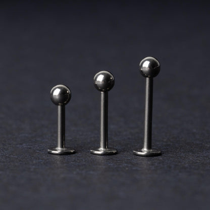 Three silver stainless steel labret studs with flat backs and polished ball ends, displayed on a dark textured background.