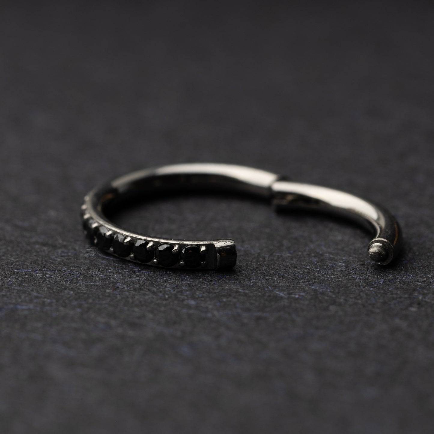 A textured stainless steel seamless ring with a polished finish, placed on a dark, textured background.