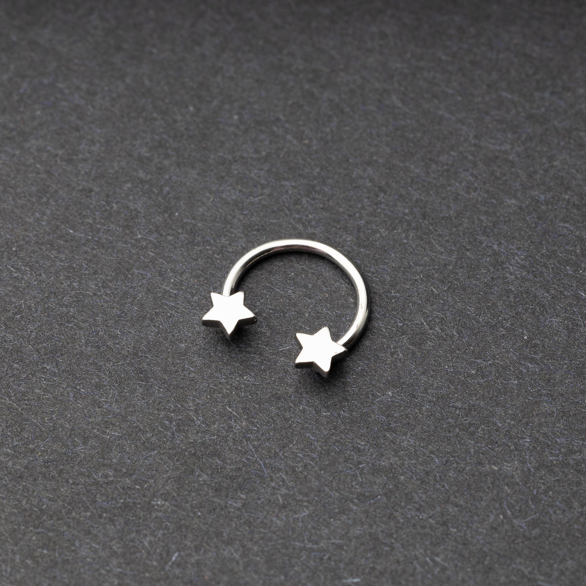 Stainless steel horseshoe hoop with star-shaped ends displayed on a dark background.