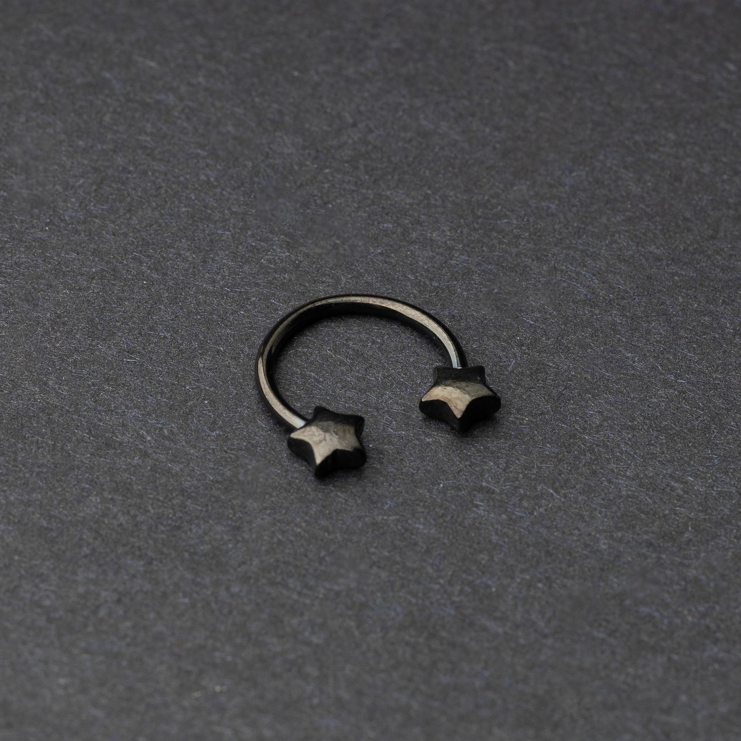 Stainless steel horseshoe hoop with star-shaped ends in black, displayed on a dark background.