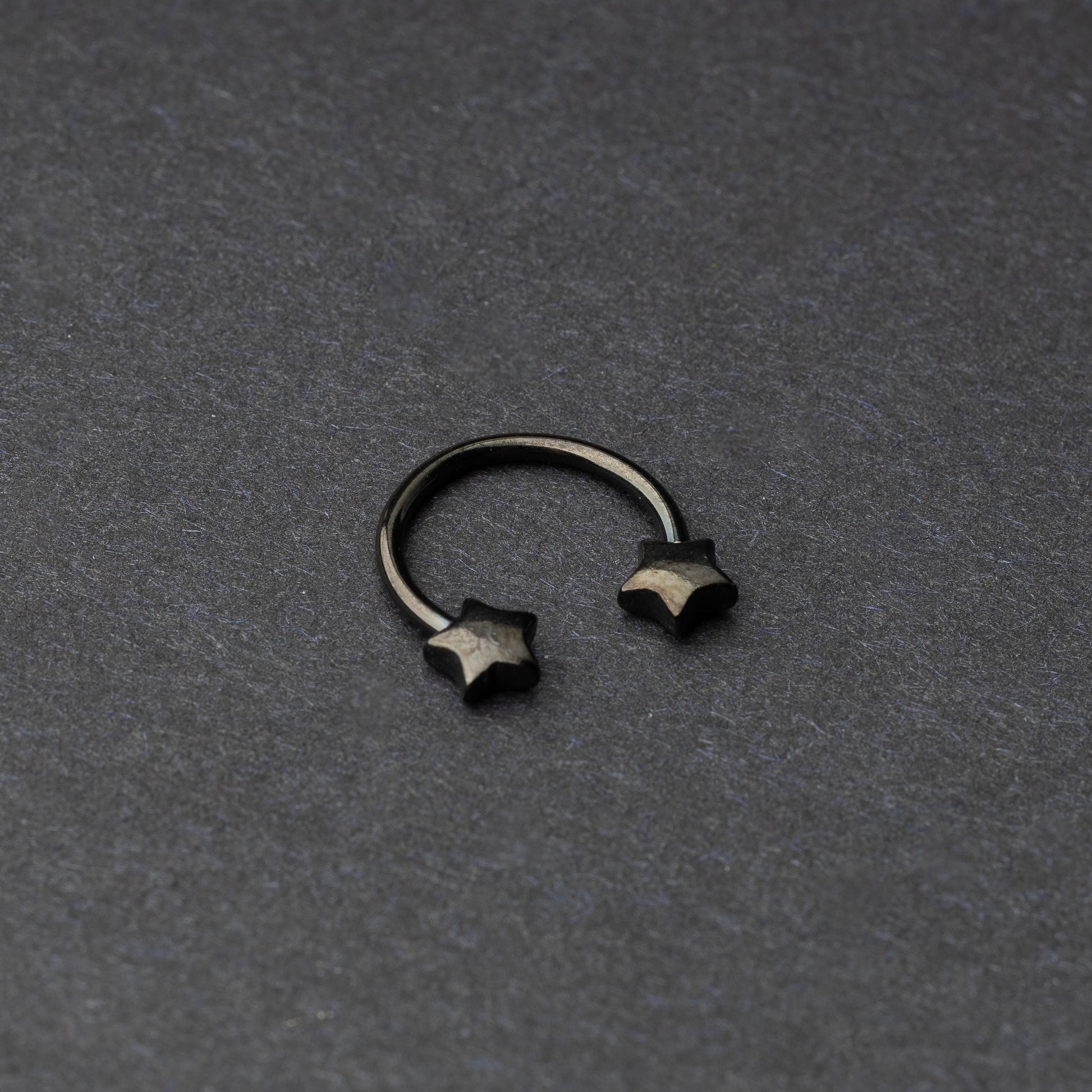 Stainless steel horseshoe hoop with star-shaped ends in black, displayed on a dark background.