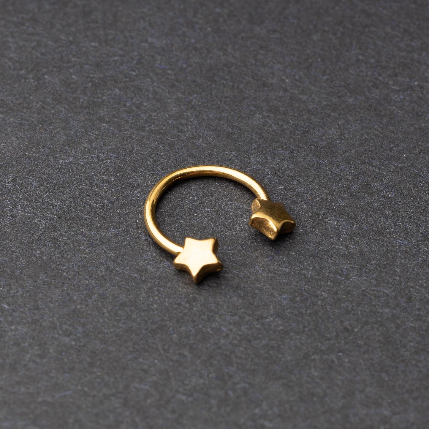 Stainless steel horseshoe hoop with star-shaped ends in gold, displayed on a dark background.