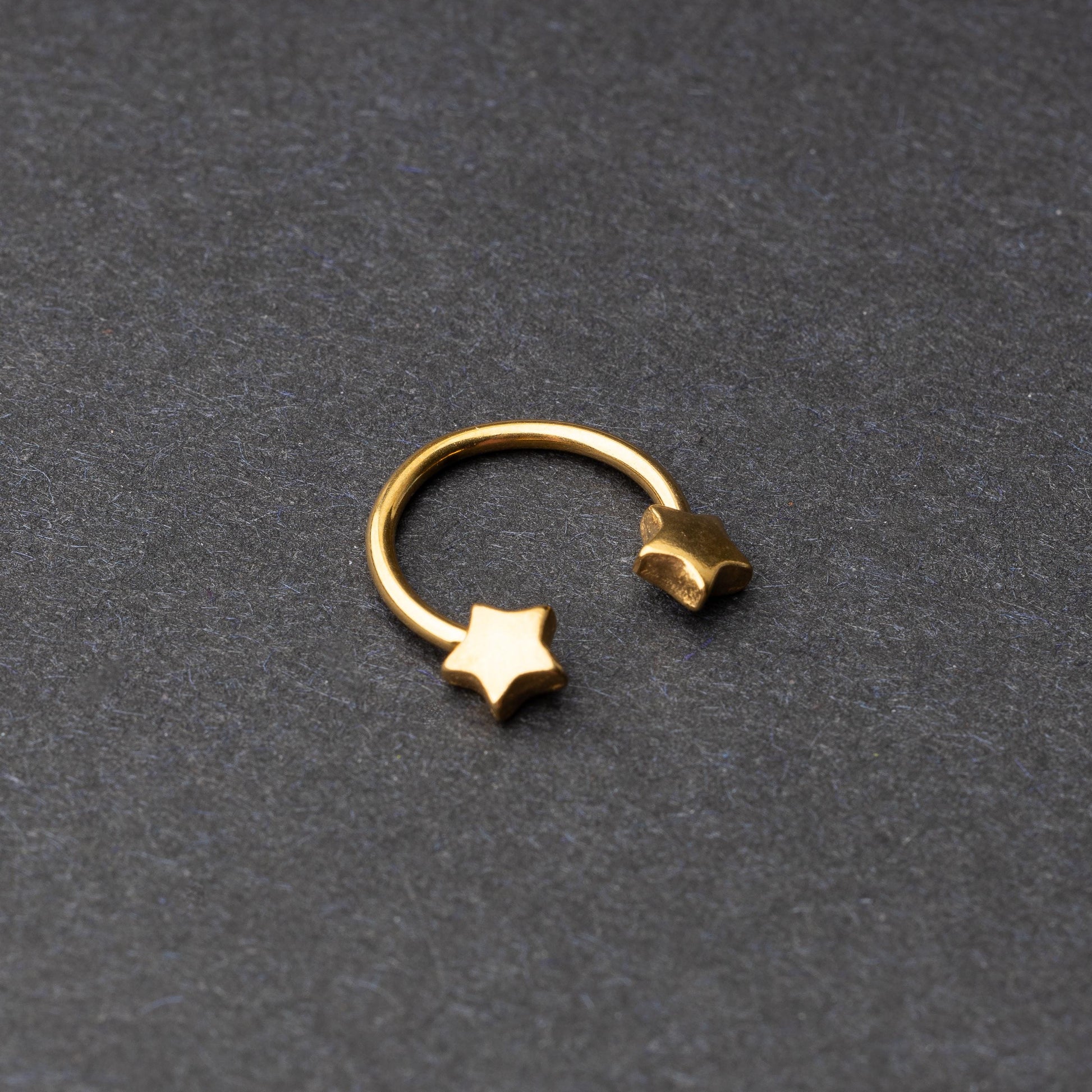 Stainless steel horseshoe hoop with star-shaped ends in gold, displayed on a dark background.
